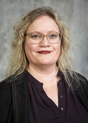 Porträttfoto av Sara Kärrholm. Hon har långt blont hår, glasögon och bär en svart blus.