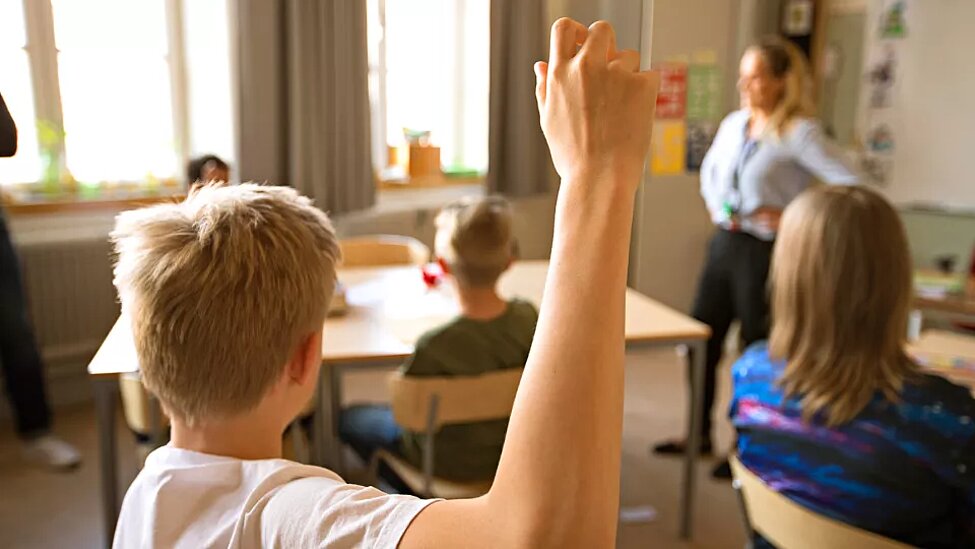 Bild från ett klassrum med barn från grundskolan.En räcker upp handen.