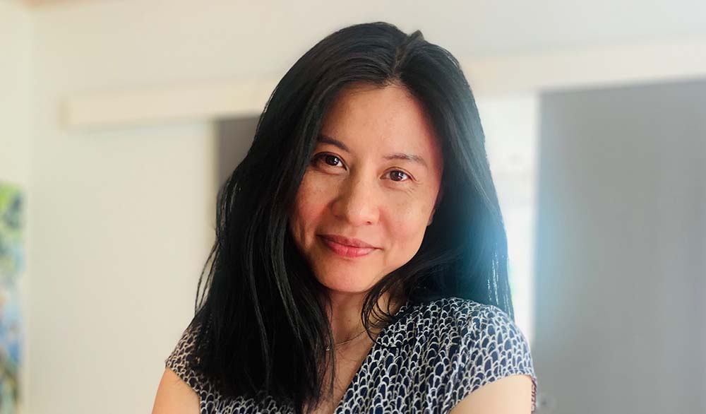 Lu Yi Nilsson, Internationella kontoret vid Samhällsvetenskapliga fakulteten ALT-text: Lu Yi har bruna ögon och svart hår som faller fram över ena axeln. Hon tittar rakt in i kameran. Hon står med armarna i kors i ett ljust rum, ett fönster skymtar i bakgrunden. Hon har på sig en svartvitmönstrad, V-ringad blus
